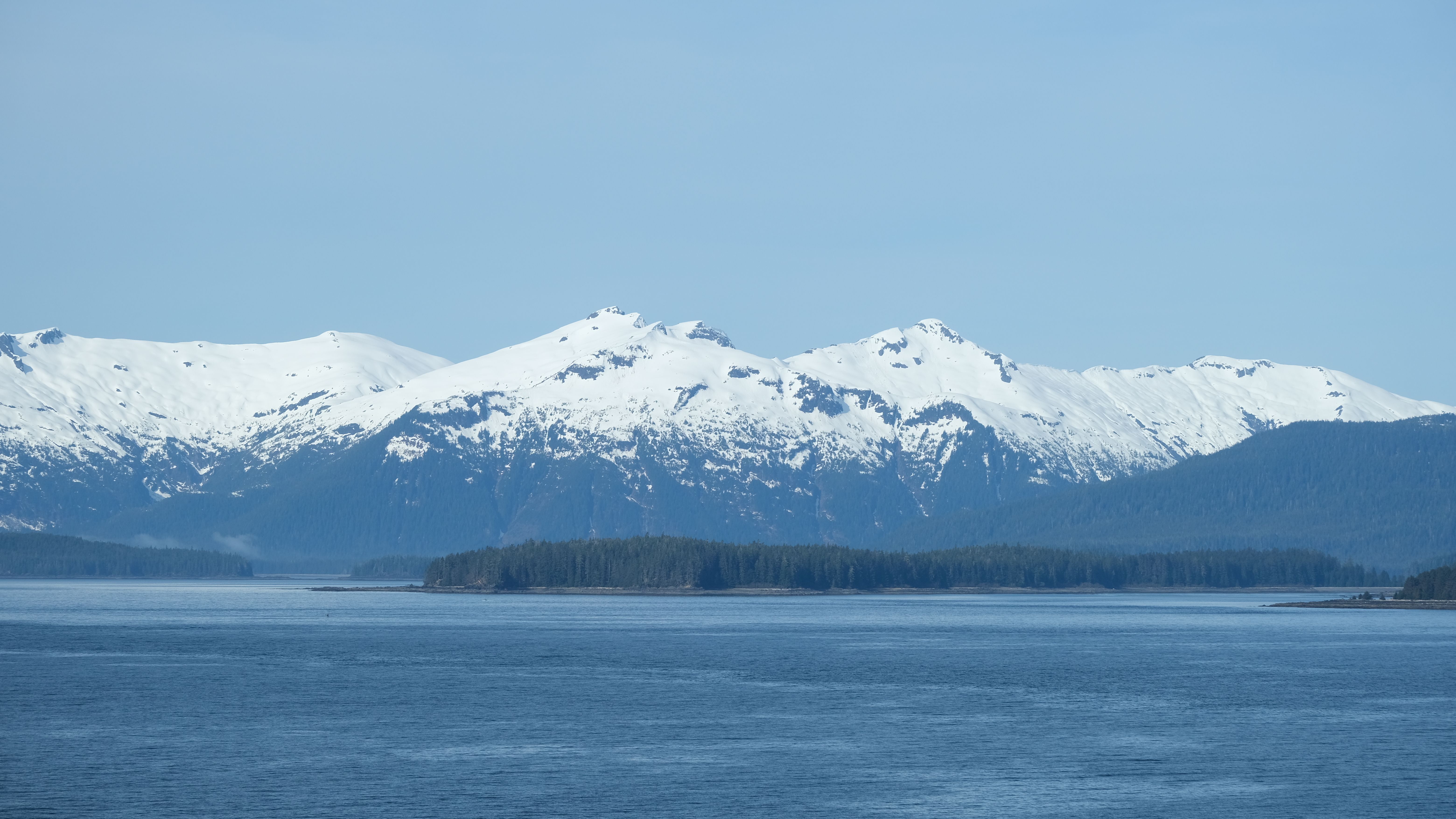 Tidewater glacier calving into the sea with snow-capped mountains in Alaska
